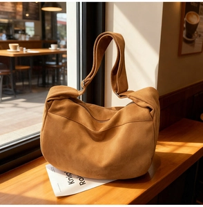 Brown suede hobo bag shown in a cozy cafe setting with natural sunlight detail