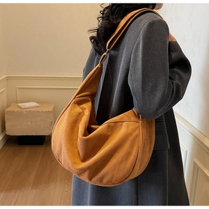 Detailed side view of a large caramel suede crescent bag worn on a model's shoulder