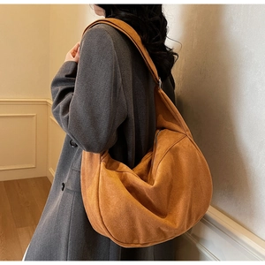 Detailed view of the brown crescent hobo bag in suede texture worn over a wool coat