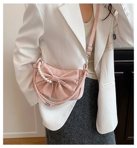 Dettaglio borsa a tracolla rosa con fiocco e catena di perle su un blazer bianco