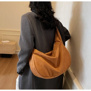 Rear view of a model wearing the large caramel suede crescent bag with a casual grey blazer