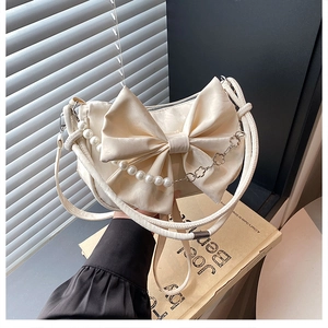 Détail du sac bandoulière en satin crème avec un grand nœud et chaîne perlée