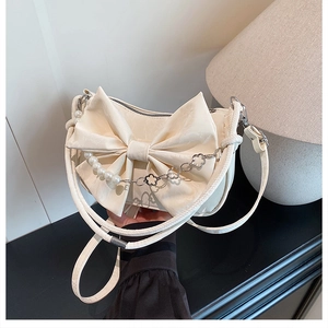 Détail d'un sac à main blanc crème avec nœud, perles et accents de chaîne en fleur