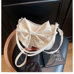 Détail d'un sac crème avec nœud décoratif et chaîne en perles sur tabouret noir