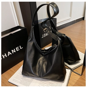Detail of a black leather tote bag with stitching and adjustable strap on a mirror surface