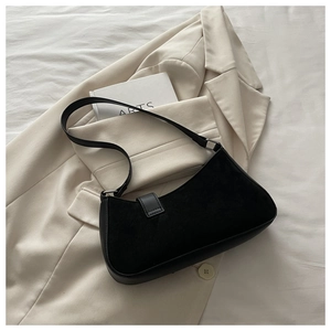 Detail of minimalist black suede crescent bag placed on a chic beige blazer