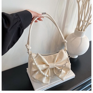 Détail du sac crème avec un grand nœud et une chaîne de perles en trèfle élégant