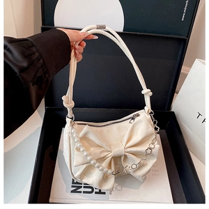 Détail du sac à main blanc crème avec nœud, chaîne de perles et bandoulière trèfle
