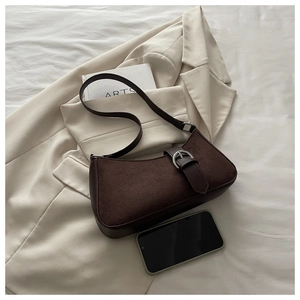 Detailed close-up of dark brown suede crescent bag with silver buckle on beige suit jacket
