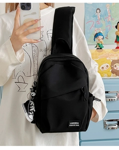 Détail du sac bandoulière en toile noire avec étiquette mode et pendentif baskets