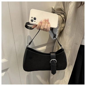 Detail of black suede crescent bag with leather trim and silver buckle held by a model