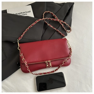 Macro detail of red lychee leather handbag with gold chain strap next to a smartphone