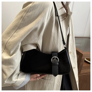 Detail of minimalist black crescent bag with silver buckle worn over a beige trench coat