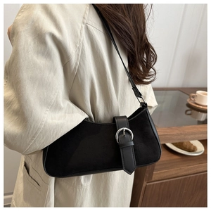 Detail of black suede underarm bag with silver horseshoe buckle on a beige trench coat