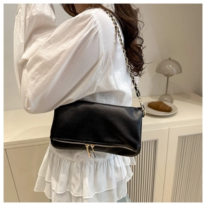 Detail of black lychee textured shoulder bag with gold chain strap and dual zippers