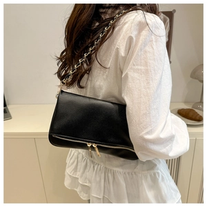 Detail of black lychee pattern shoulder bag with metal chain strap on model