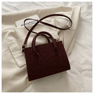 Detail view of burgundy leopard print square handbag on a beige suit jacket fabric