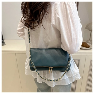 Deep green pebble leather crossbody bag with gold chain strap shown on model shoulder