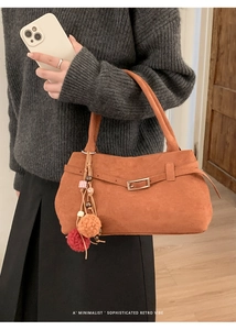 Detail of terracotta suede tote bag with decorative strap and colorful pompom charm
