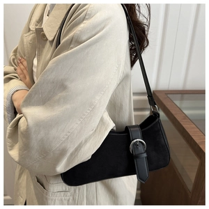 Detail of black suede underarm bag with large silver buckle on a beige trench coat