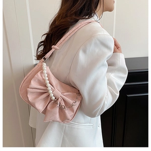 Sac sous le bras rose avec nœud, perles et chaîne argentée porté à l'épaule