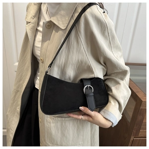 Detail of black suede crescent bag with silver buckle worn over a beige trench coat