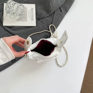 Elegant white quilted chain handbag on grey suit blazer with artistic book backdrop