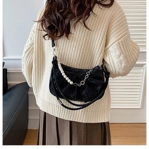 Détail du sac bandoulière noir avec nœud, sangle perlée et chaîne florale sur un pull