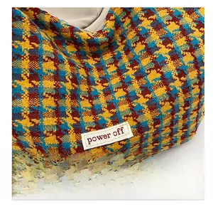 Close-up of multicolor plaid tweed fabric and embroidered power off label on dumpling bag