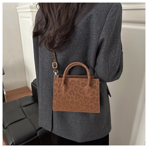 Detail of leopard print crossbody bag worn with a grey blazer in a modern interior setting