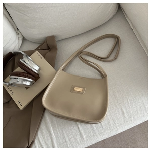Close-up of beige faux leather shoulder bag with gold metal logo on a textured sofa