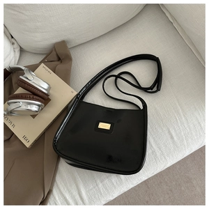Detail of a black glossy shoulder bag with a gold metal plate on a cozy sofa