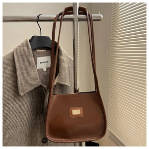 Detail of a brown leather shoulder bag with a gold square metal plate on a hanger