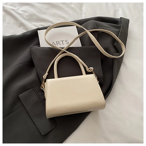 Close-up of a cream minimalist crossbody bag on a black blazer with hardware detail