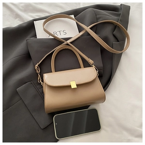 Detailed view of khaki leather crossbody bag with golden buckle on textured bedding