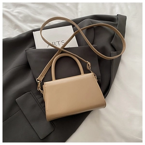 Flat lay of camel vintage crossbody bag on white fabric with fashion magazine