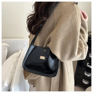 Detail of glossy black patent leather shoulder bag with gold metal plate logo