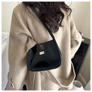 Detail view of a black glossy underarm bag with gold metal plaque worn on the shoulder