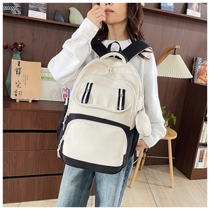 Detail of canvas backpack featuring multi-pocket design and stylish round pendant accessory
