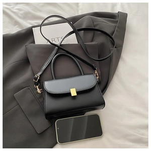 Flat lay of a black minimalist leather bag with golden square lock and adjustable strap
