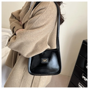 Detail of a retro black shiny leather rectangular shoulder bag with a gold metal plaque