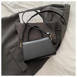 Detail view of black matte leather mini bag with gold hardware on a suit jacket