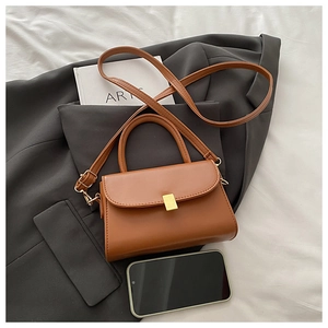 Detail view of mini brown crossbody bag with gold buckle on grey blazer and book