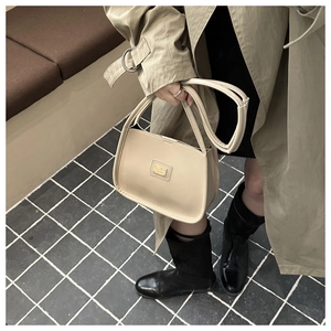 Close-up of beige minimalist handbag with gold metal logo plate and smooth leather texture