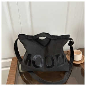 Dettaglio di una borsa in tela nera con scritta MOOD lucida e fibbia in metallo regolabile