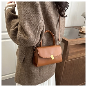 Detail of caramel brown leather handbag with gold clasp worn over a brown blazer