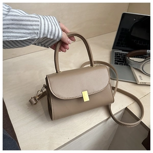 Detail view of khaki square crossbody bag with gold metallic lock on a wooden desk