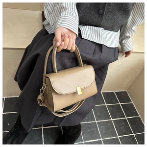 Detail of khaki leather handbag with gold rectangular buckle and top handle held by a model