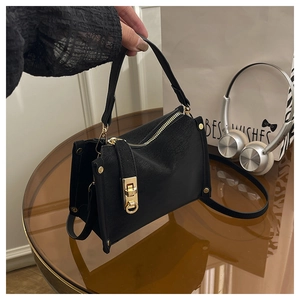Detail of a chic black square handbag with golden hardware on a stylish glass table