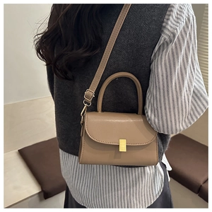 Detailed view of beige crossbody bag with gold buckle and adjustable strap on a model